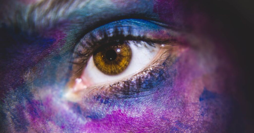 A vibrant close-up of a human eye surrounded by colorful paint, showcasing artistic expression.