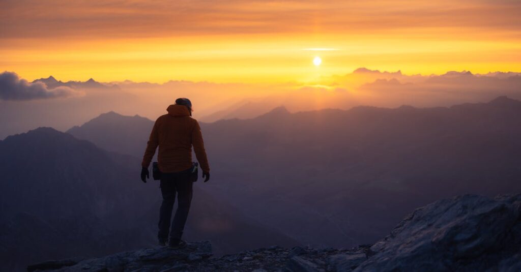 A lone hiker silhouetted against a vibrant mountain sunrise.
